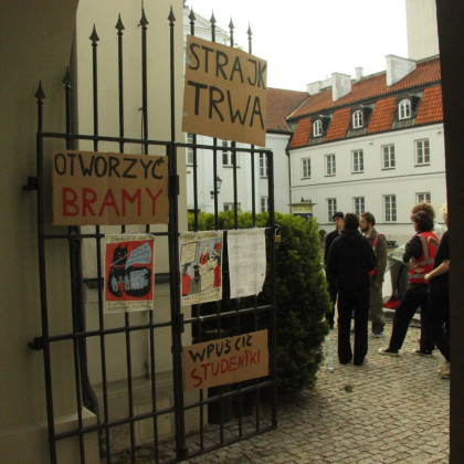 Slika železnih vrat a, ki vodijo na dvorišče stavbe Študentskega sveta Univerze v Varšavi. Na vratih so protestni slogani zasedbe.