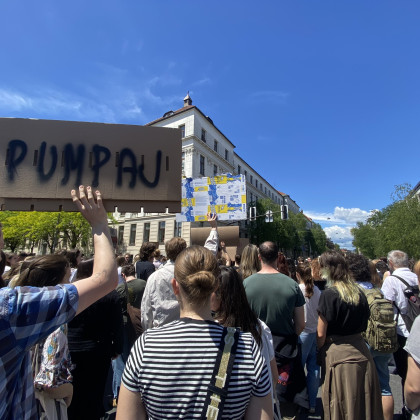 Fotografija večjega števila protestnikov, eden od njih drži kartonast transparent, na katerem z velikimi tiskanimi črkami piše pumpaj