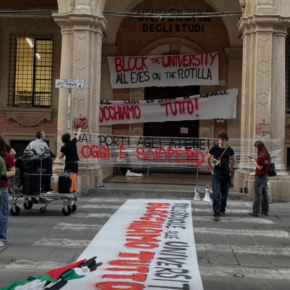 Slika vhoda v eno izmed stavb Univerze v Bologni čez vhod katere so na transparentih obešeni slogani študentske stavke.