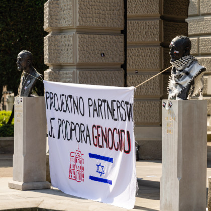 Slika z majskega protesta LDŠ pred rektoratom Univerze v Ljubljani. Na sliki je za doprsna kipa obešena zastava, na kateri piše "Projektno partnerstvo je podpora genocidu". Pod napisom sta narisana logotip Univerze v Ljubljani in izraelska zastava.
