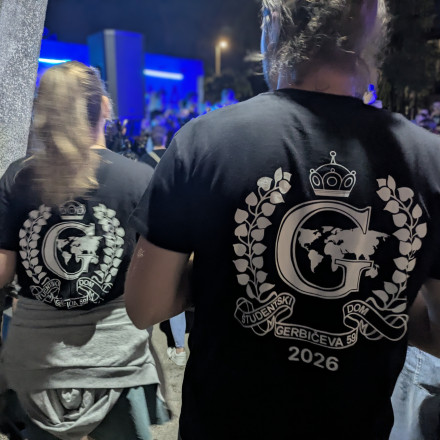 Na sliki sta na hrbtu majice dveh obiskovalcev dnevom doma Gerbičeve 59 vidna logotipa doma. V ozadju je videti glasbeni oder, na katerem igra bend.