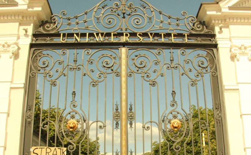 Slika velikih znanjih vhodnih vrat na Univerzo v Varšavi, na katera so pritrjene table s protestnimi napisi.