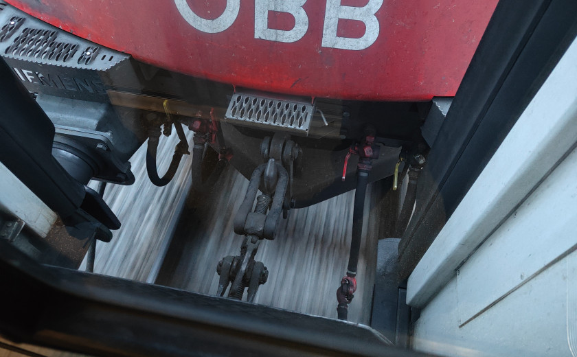 öbb lokomotiva, na katero je priklopljen hrvaški vagon, v ozadju se vidi stran brzeča tla