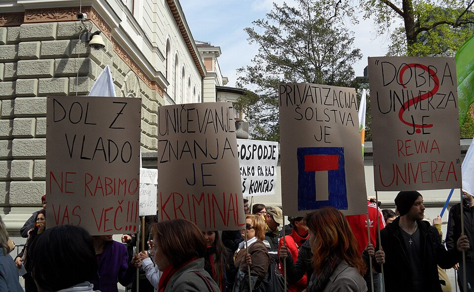 Splošna stavka javnega sektorja pred vladno palačo, aprila 2012. Na transparentih je od leve proti desni napisano "Dol z vlado ne rabimo vas več", "Uničevanje znanja je kriminal", "Politizacija šolstva je [slepa ulica]", "Dobra univerza je revna univerza?".