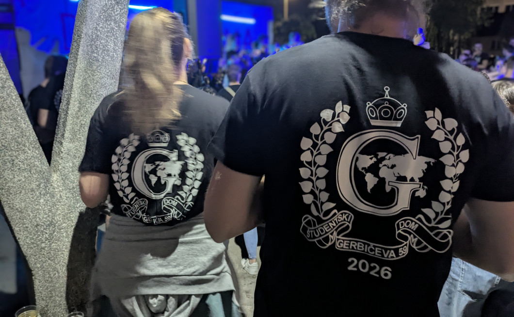 Na sliki sta na hrbtu majice dveh obiskovalcev dnevom doma Gerbičeve 59 vidna logotipa doma. V ozadju je videti glasbeni oder, na katerem igra bend.